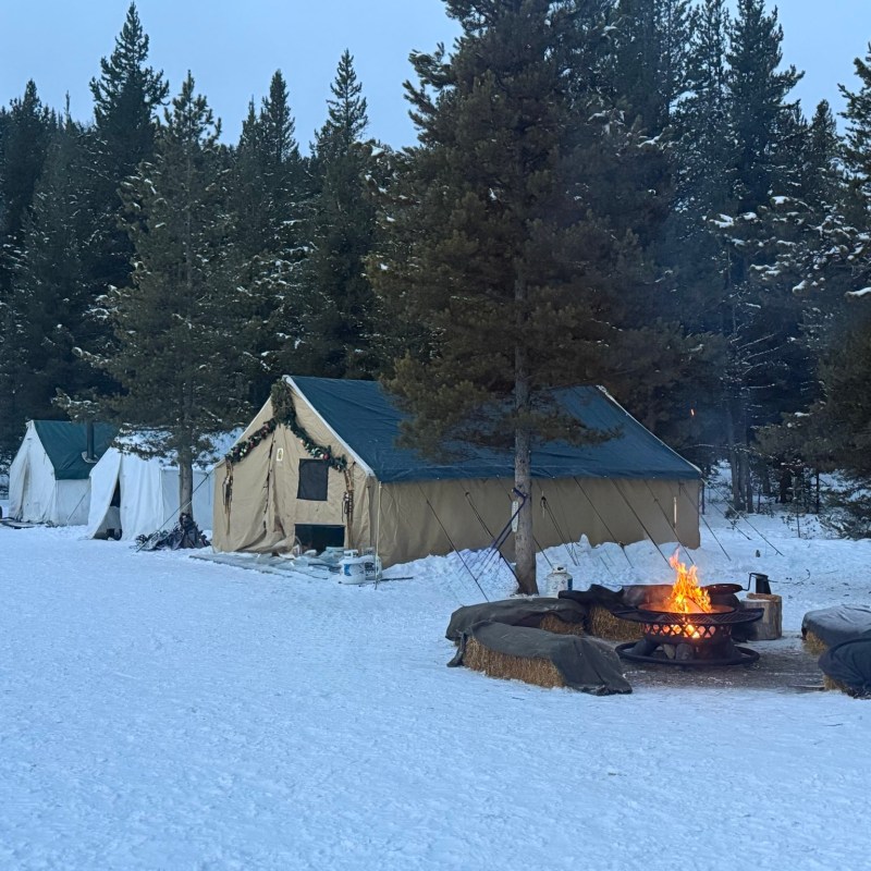 Snowy campsite with a fire pit, tents, and surrounding pine trees.